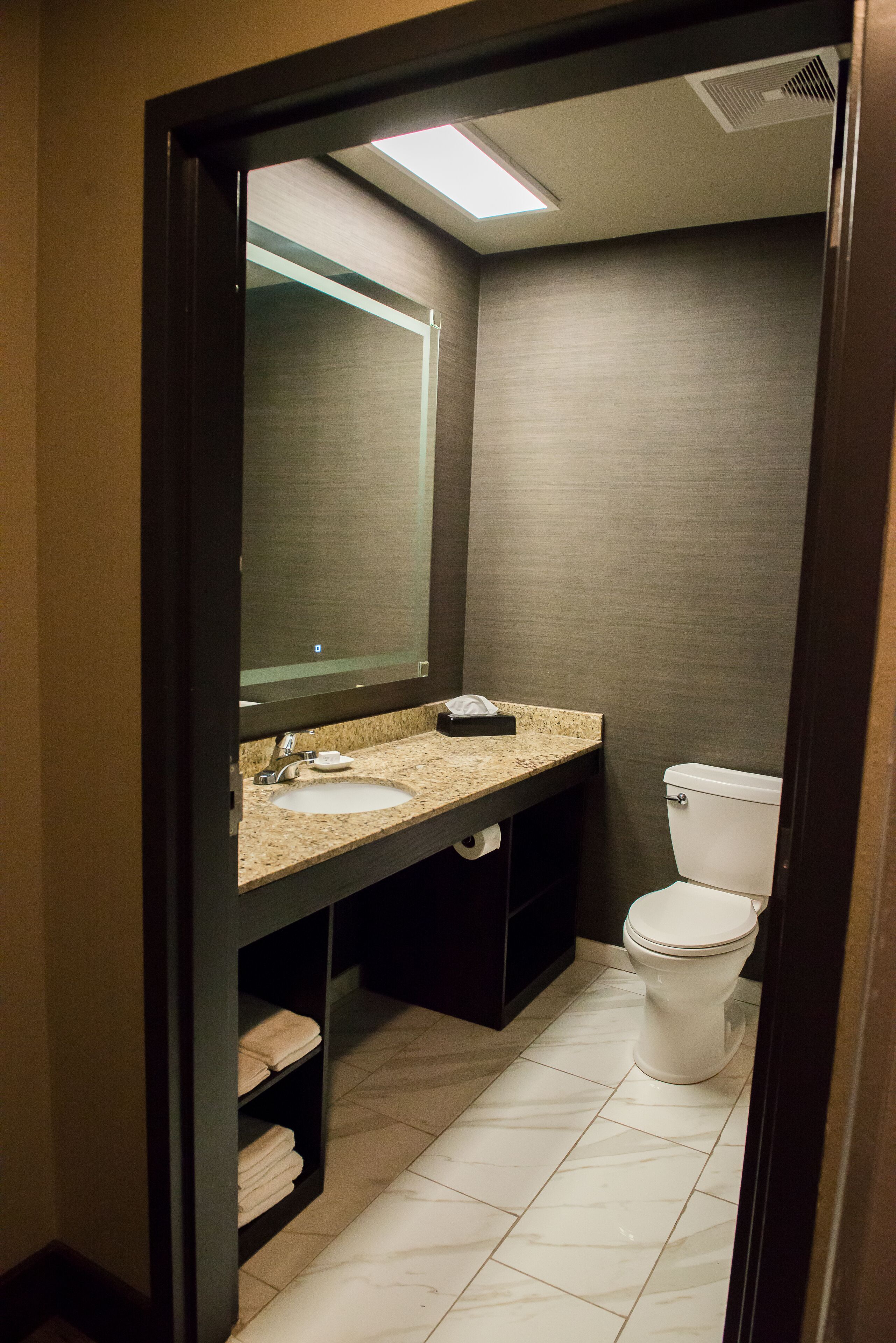 A bathroom with a sink, mirror, toilet, and shelves with towels.