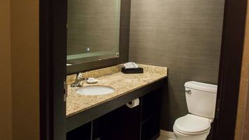 A bathroom with a sink, mirror, toilet, and shelves with towels.