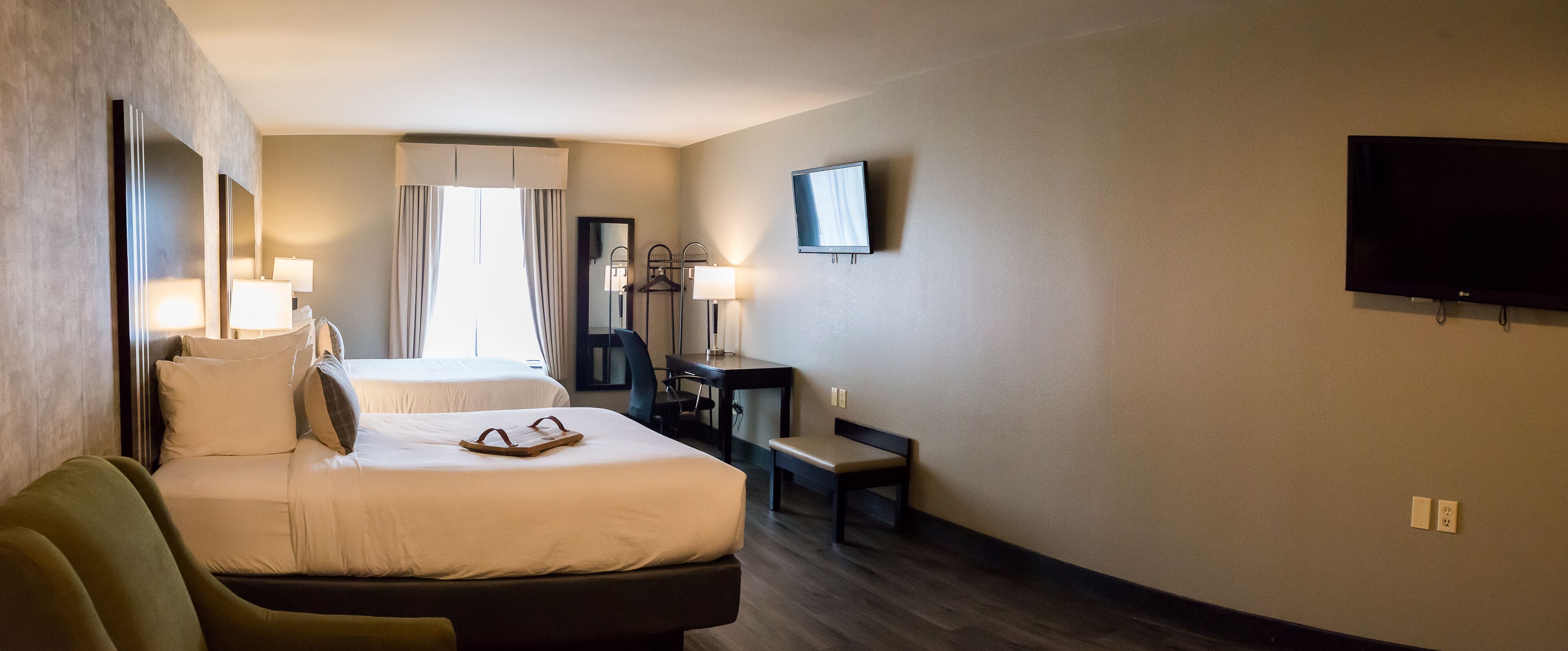 Quarto de hotel com duas camas, uma escrivaninha, uma cadeira, uma televisão e um espelho.