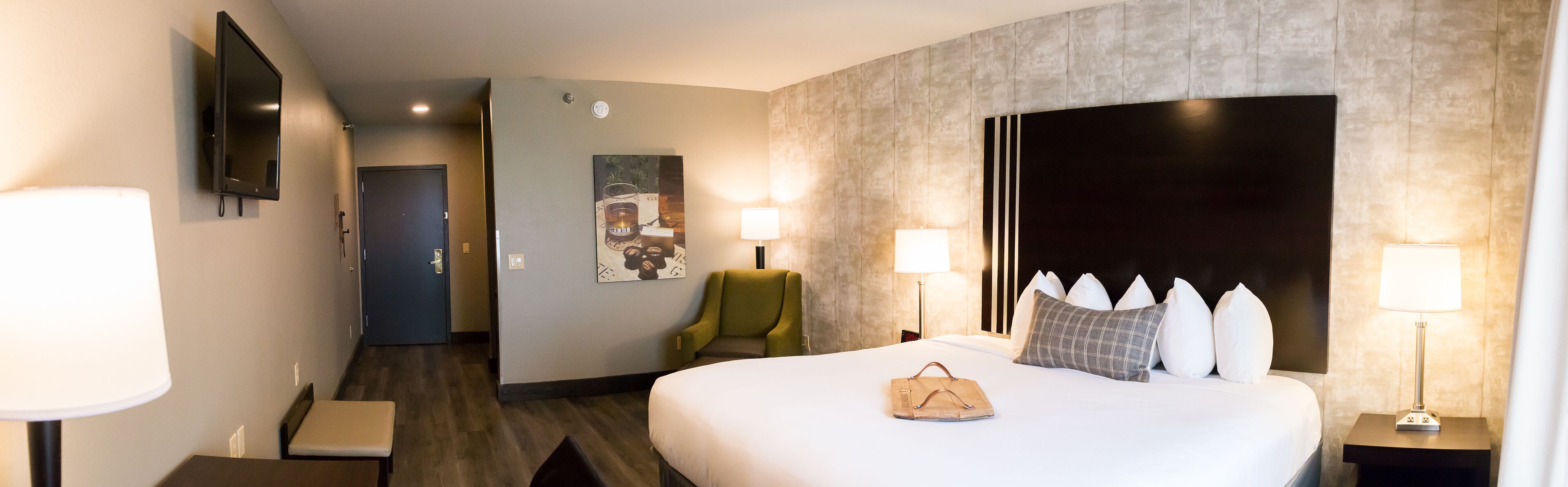 Ein Hotelzimmer mit Bett, Nachttischlampen, einem Sessel, einem Schreibtisch und einem Fernseher.
