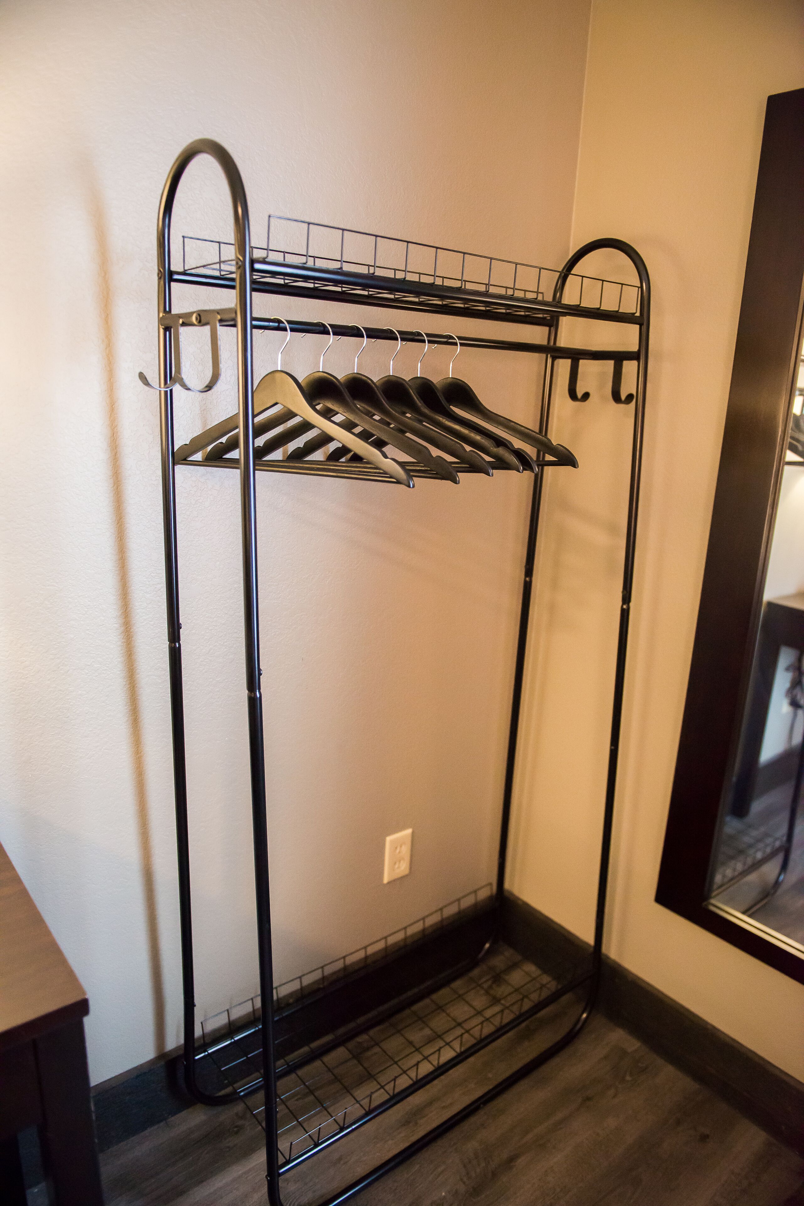 A metal coat rack with multiple hooks against a wall, a small shelf, and a power outlet below.