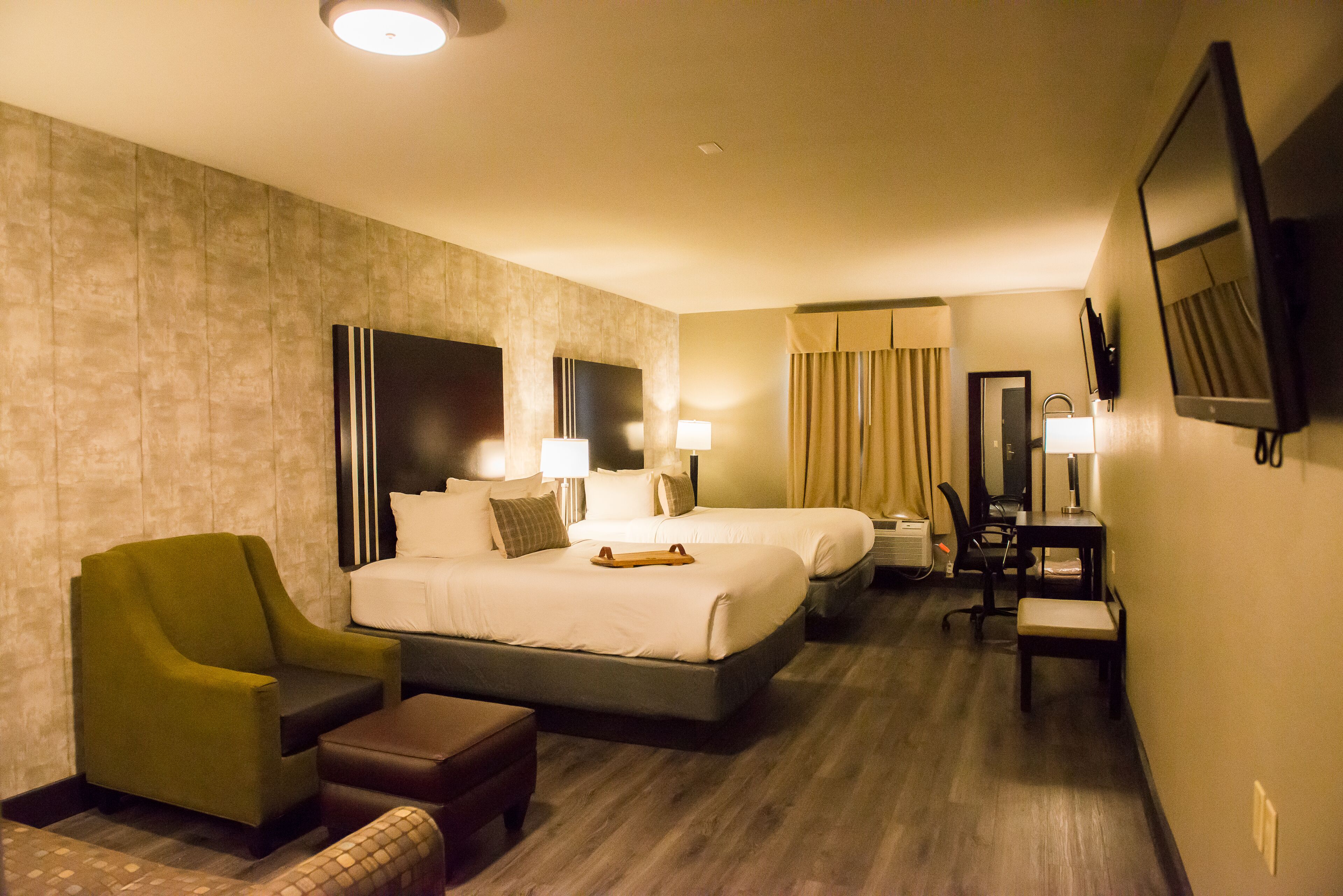 A hotel room with two beds, a desk, a chair, and a small sofa.