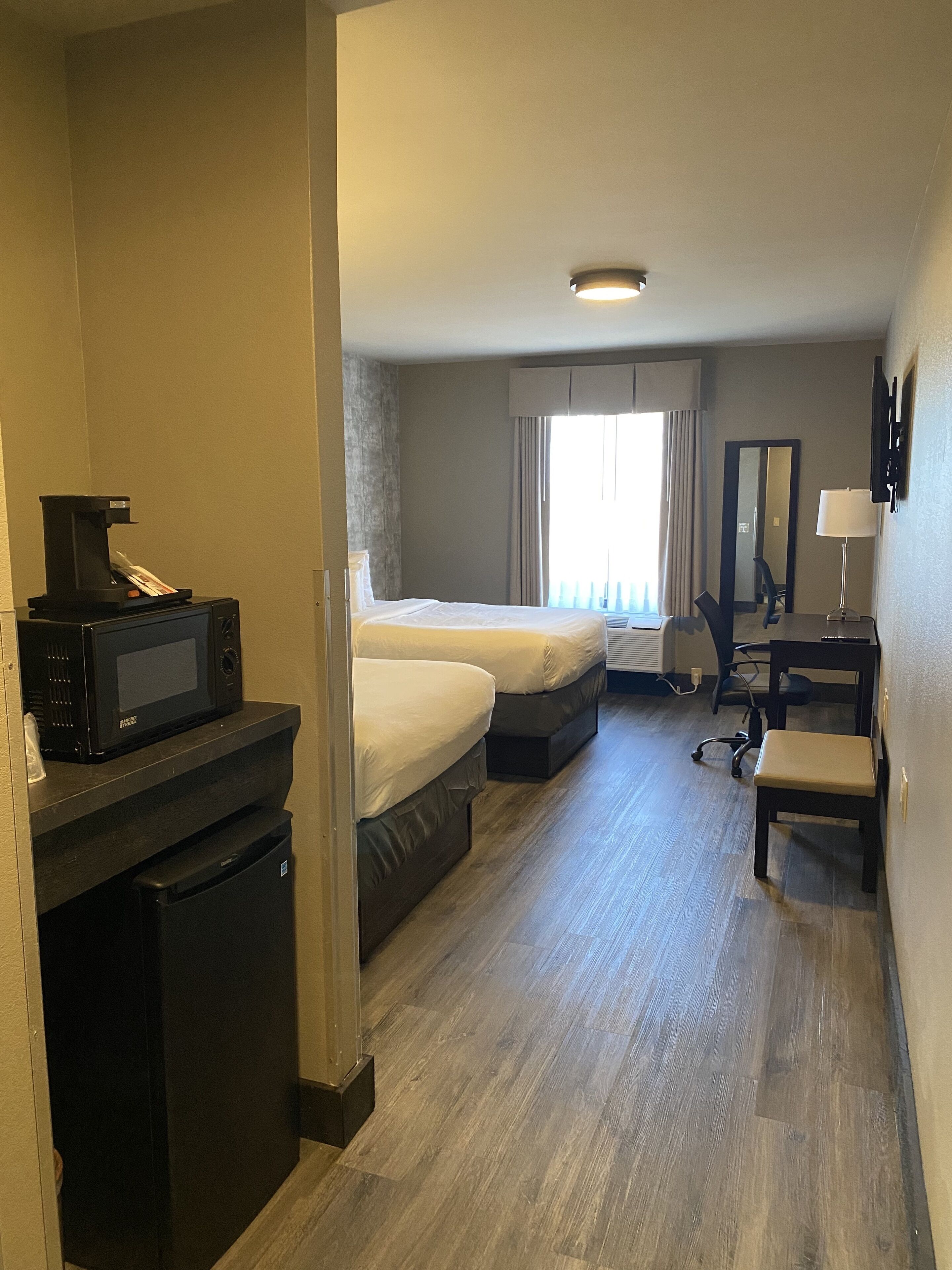 Una habitación de hotel con cama, escritorio, silla, microondas y refrigerador pequeño.