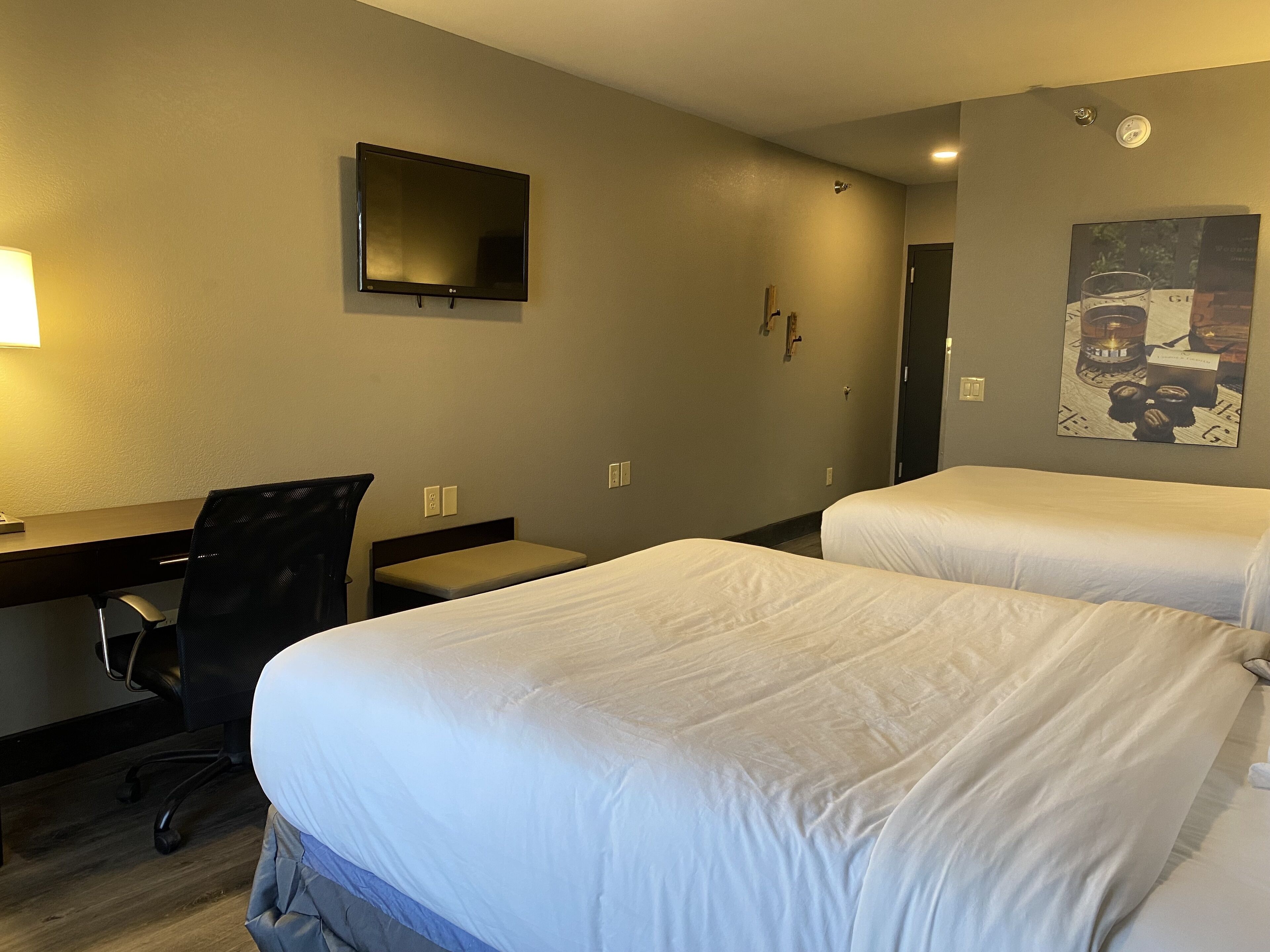 A hotel room with two beds, a desk, a chair, a TV, and a painting on the wall.