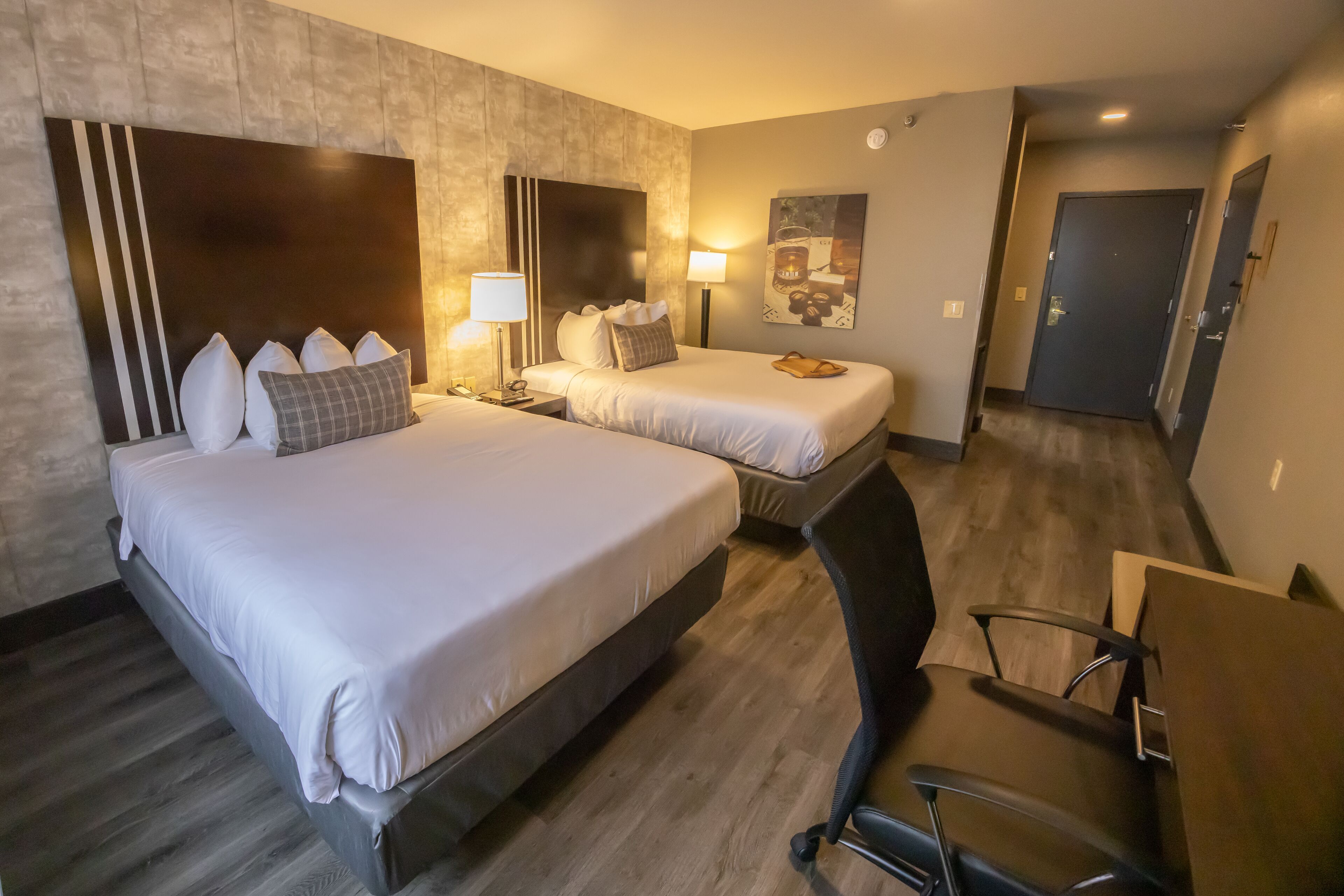 Een hotelkamer met twee bedden, een bureau en een stoel. Er staan lampen op het bureau en er hangt een schilderij aan de muur.