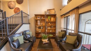A living room with two leather sofas, a coffee table, and a wooden bookshelf. A staircase is visible to the left. - Distill-Inn (Bardstown)