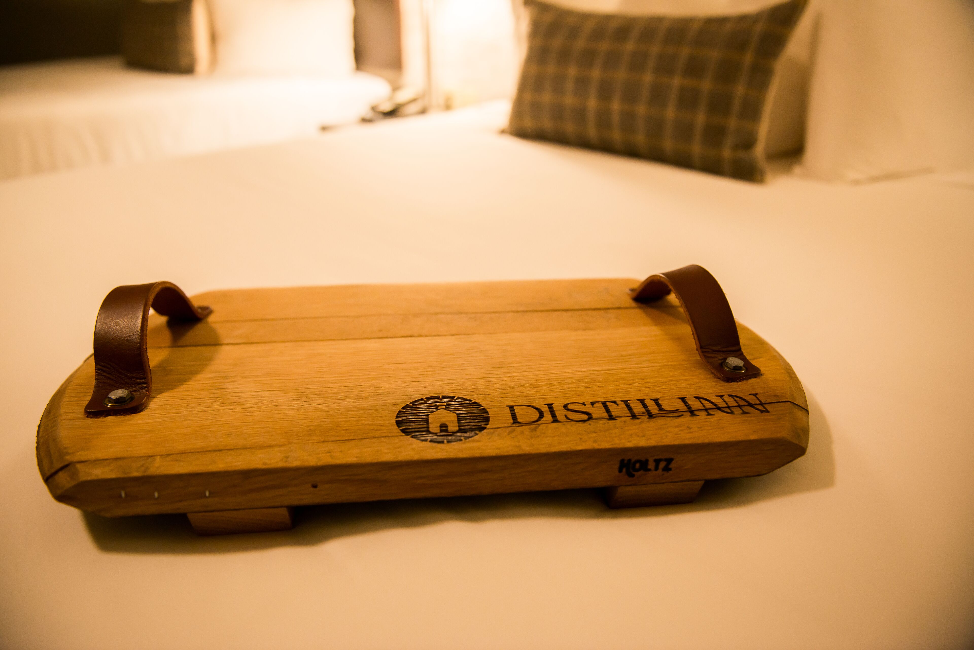 Un safata de fusta amb nanses de cuir i el text "DISTILLINN" sobre un llit.