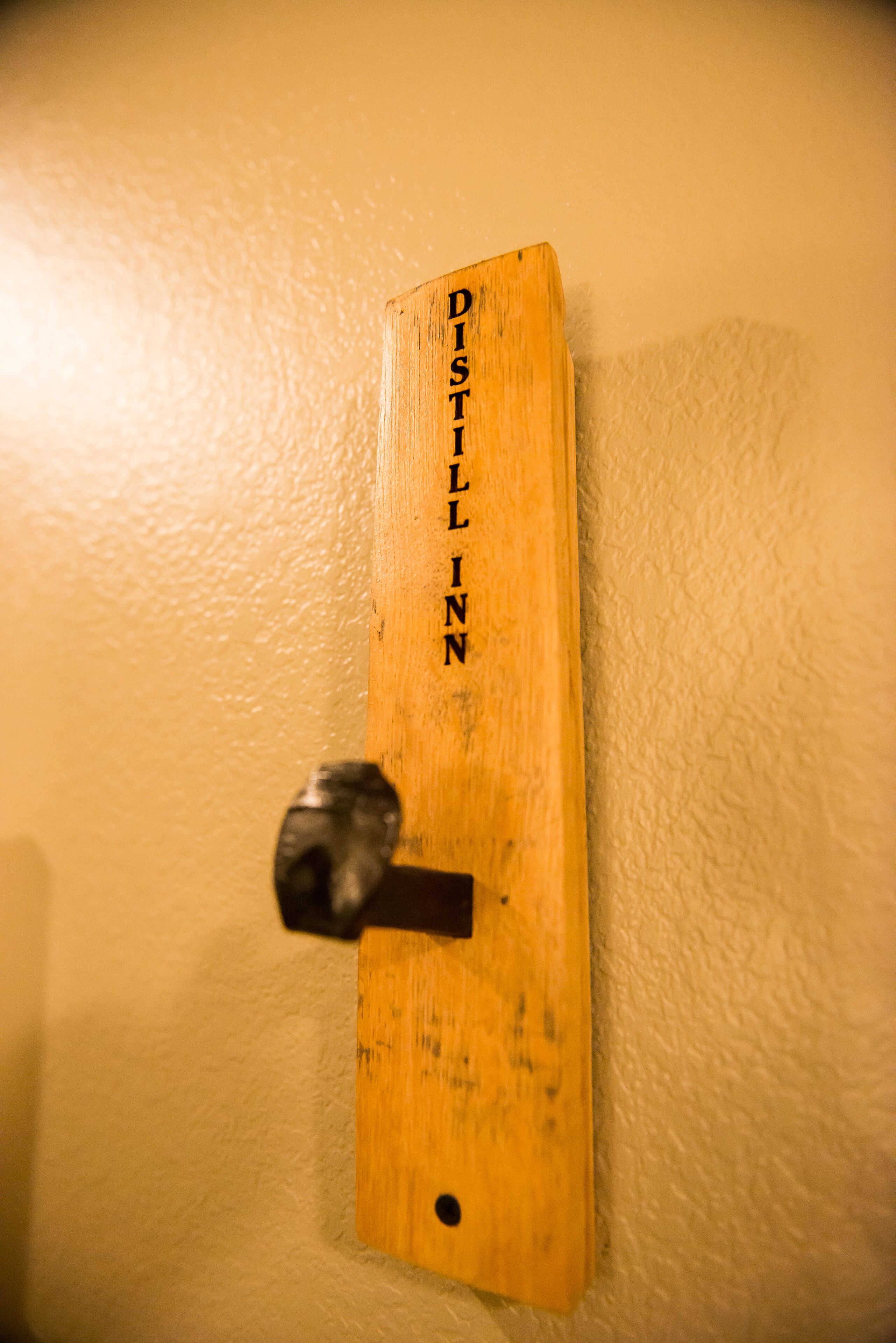 A wooden plaque with the inscription "DISTILL INN" mounted on a wall.