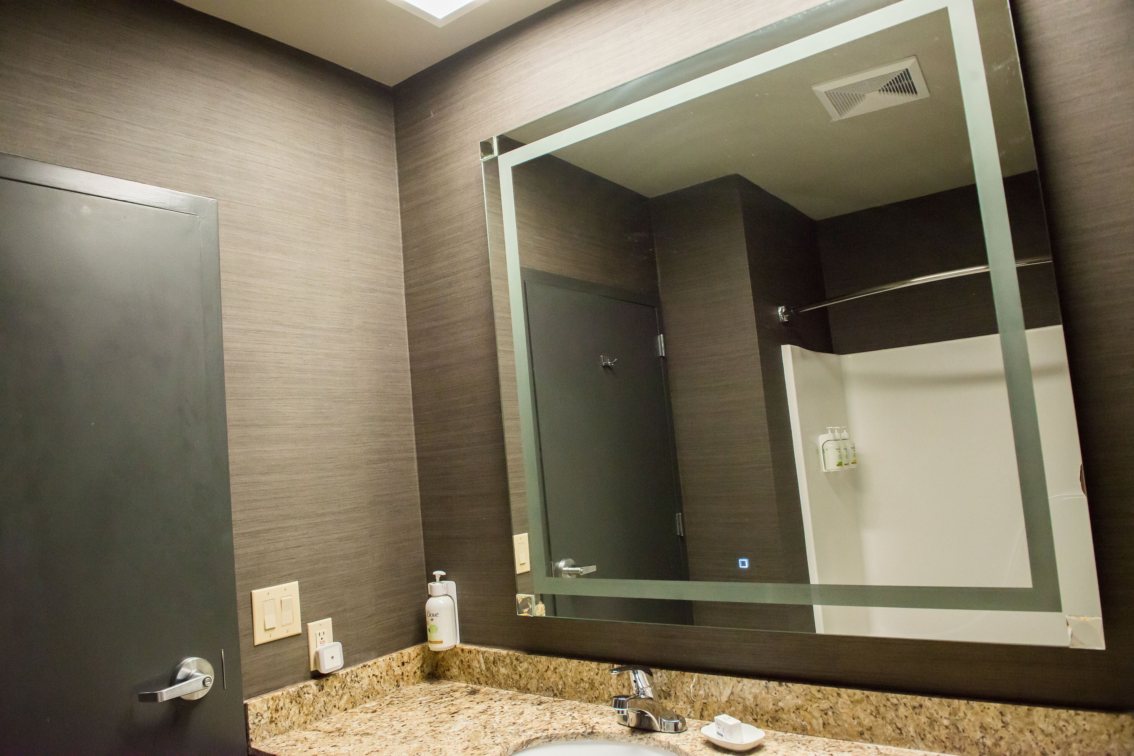 A bathroom with a large mirror, a sink, and a shower.