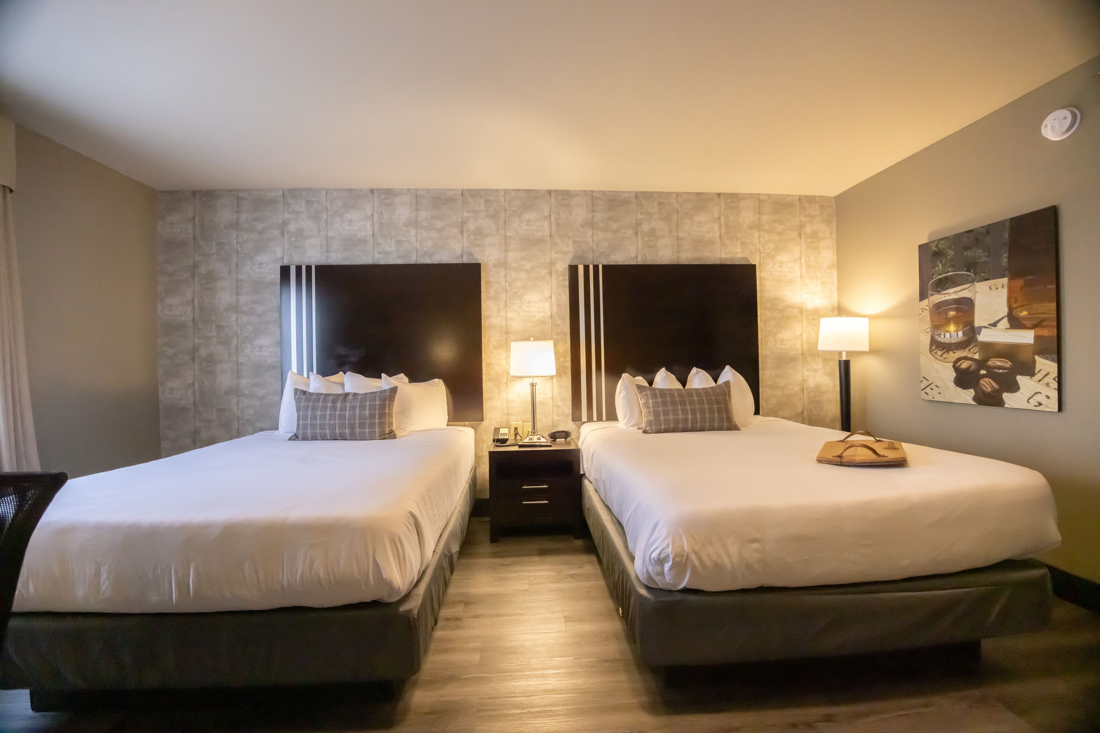 Habitación de hotel con dos camas, una mesita de noche con lámpara y un cuadro en la pared.