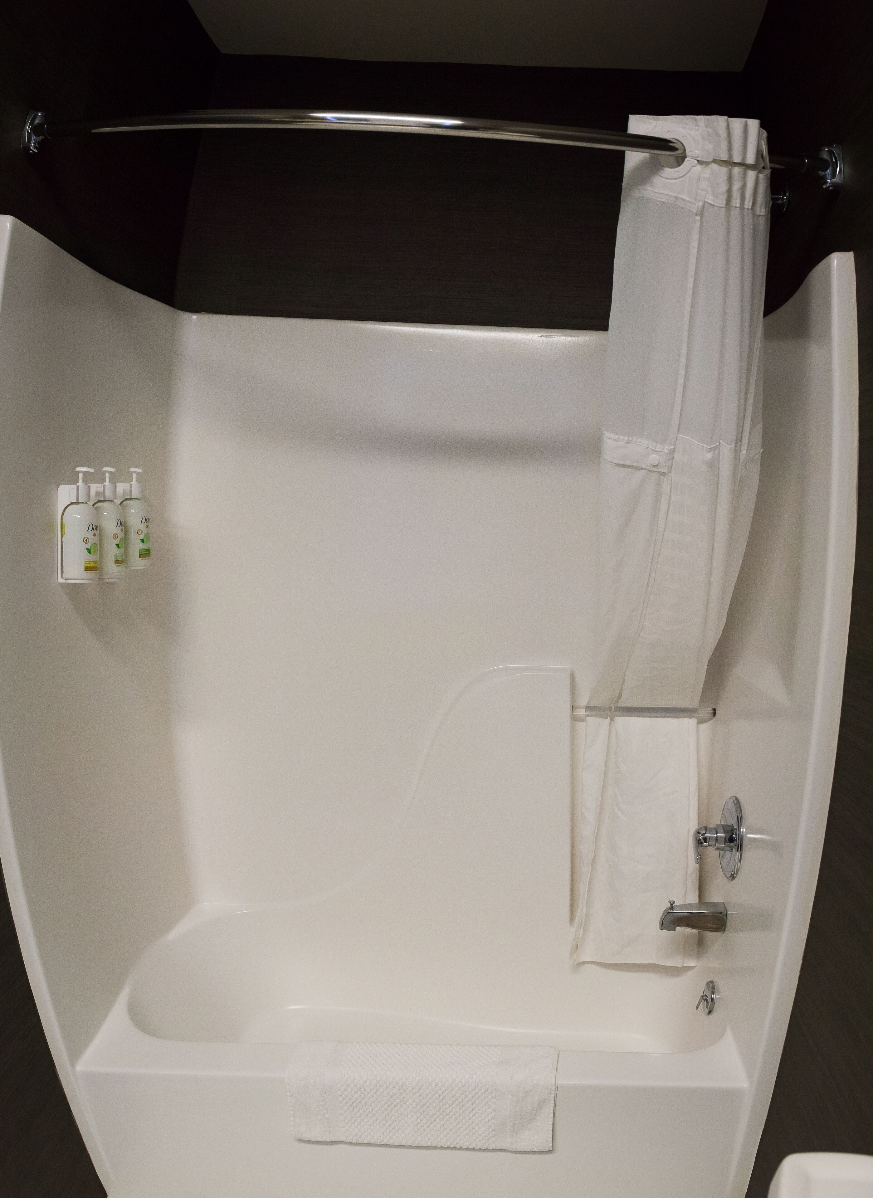 A white bathtub with a shower curtain, a towel, and three bottles of Dove body wash.