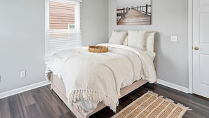Un dormitorio con cama, ventana con persianas, un cuadro en la pared y una puerta.