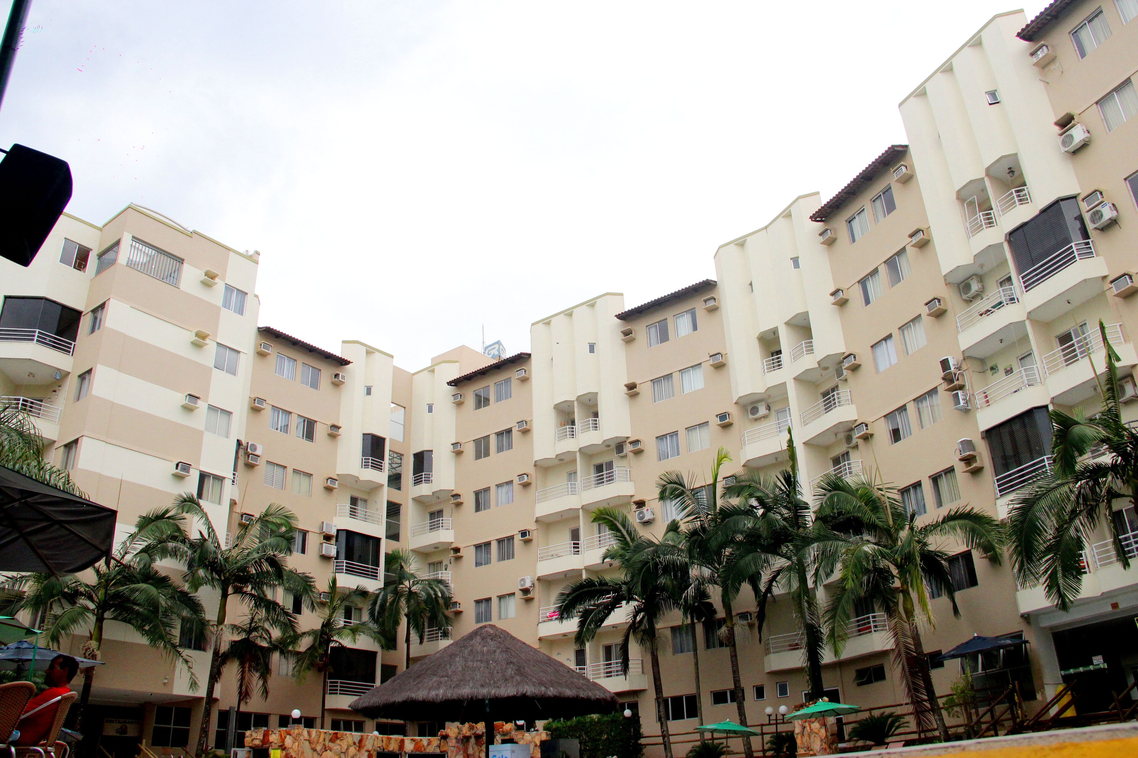 Un edificio residencial de varios pisos con balcones, equipos de aire acondicionado y palmeras.