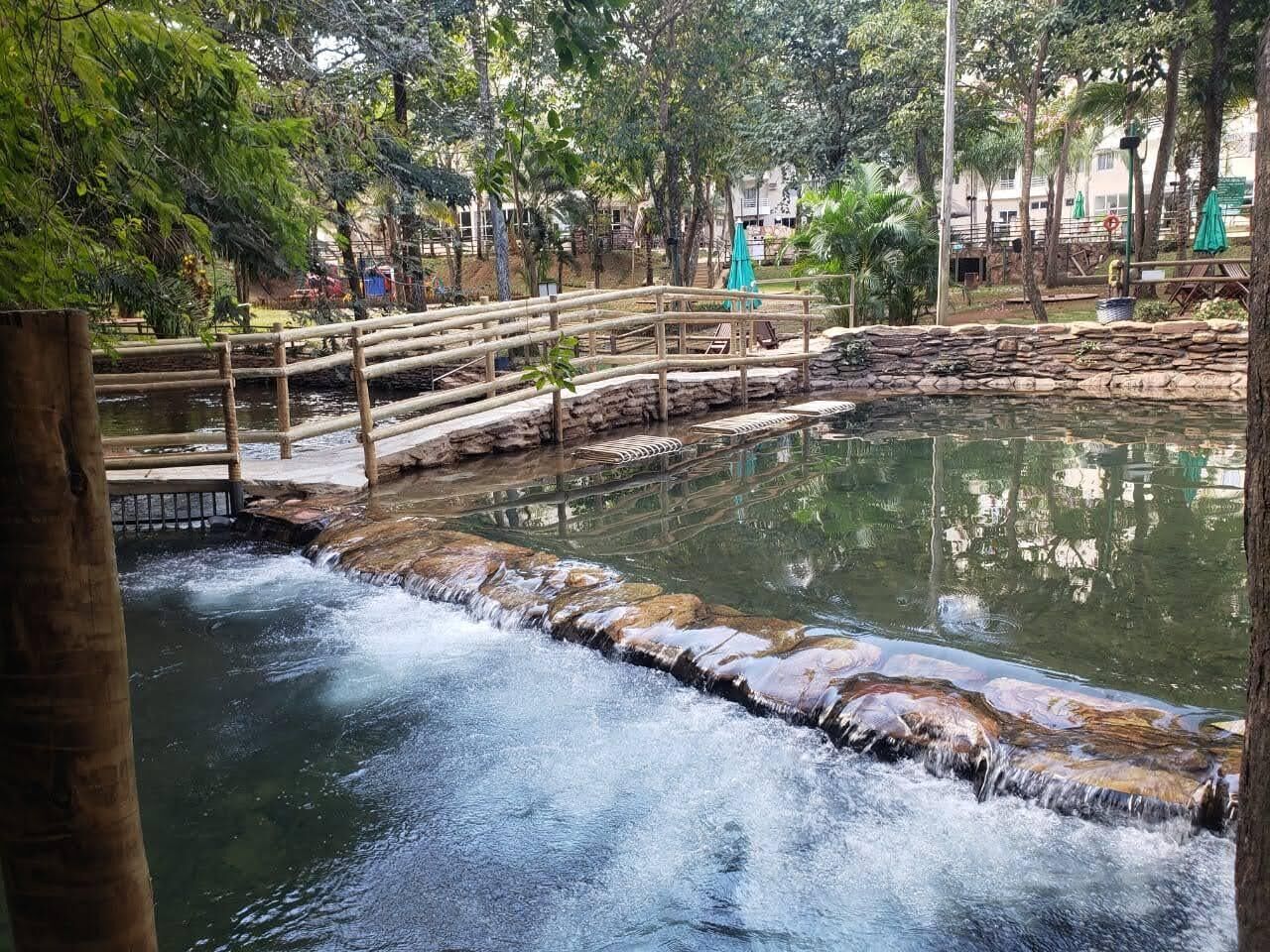 A natural water feature with a wooden bridge and seating area.