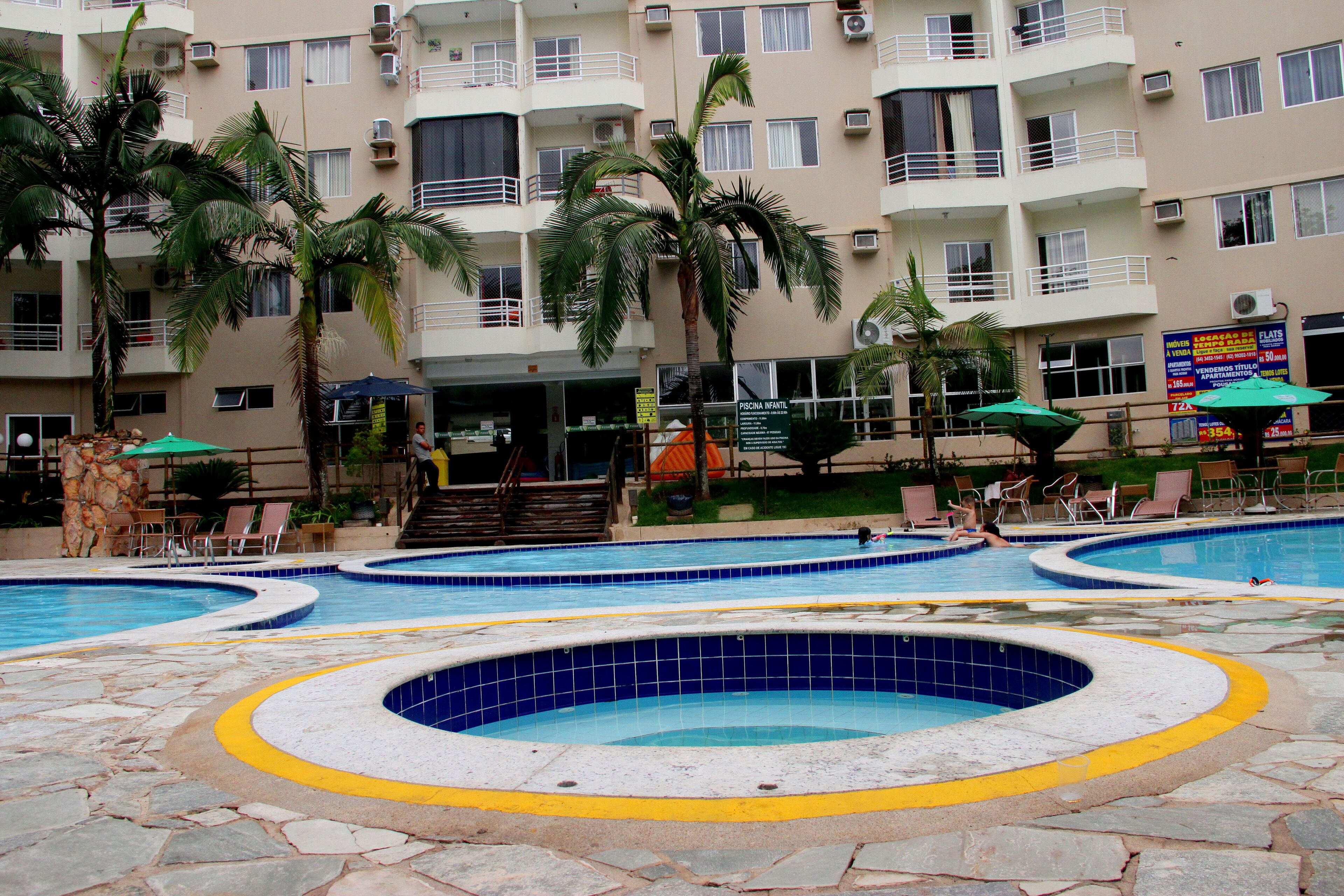A multi-level hotel with a swimming pool area, palm trees, and outdoor seating.