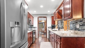 A modern kitchen with stainless steel appliances, wooden cabinets, and a stone backsplash. - Tatanka Getaway with Hot tub & Game Room (Custer)