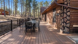 A wooden deck with outdoor furniture, surrounded by a stone wall and tall trees. - Tatanka Getaway with Hot tub & Game Room (Custer)