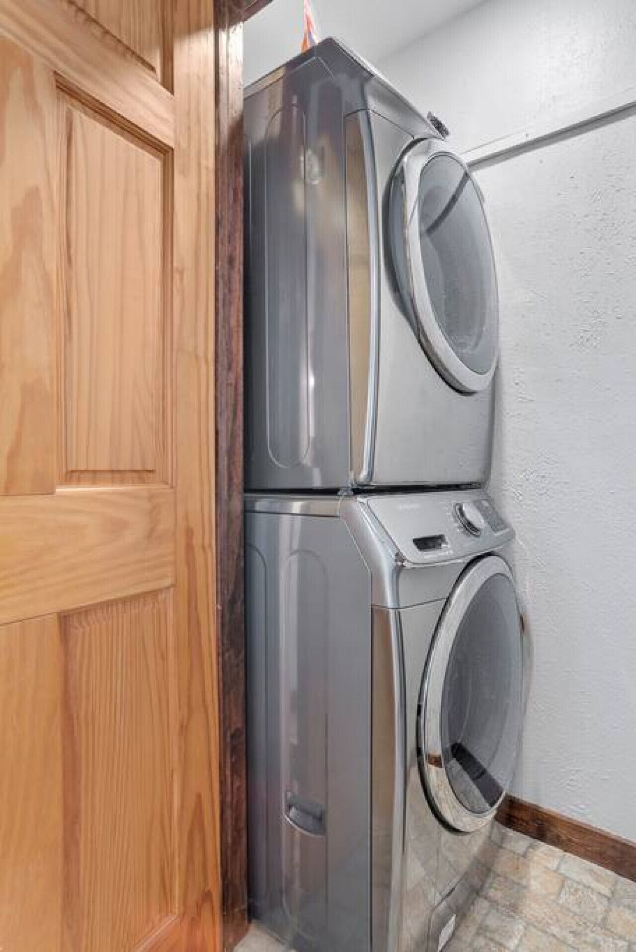 A stacked washer and dryer unit in a corner with a wooden door and a white wall.