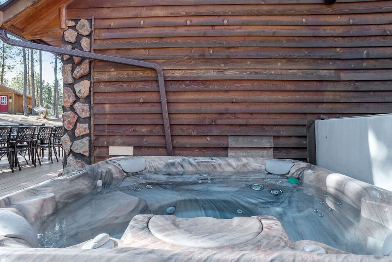 A hot tub with a stone wall backdrop, a wooden deck, and outdoor furniture.