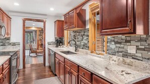 A modern kitchen with wooden cabinets, granite countertops, and a stone backsplash. - Tatanka Getaway with Hot tub & Game Room (Custer)