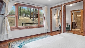 A bedroom with a large window, wooden flooring, and a view of a forest. - Tatanka Getaway with Hot tub & Game Room (Custer)