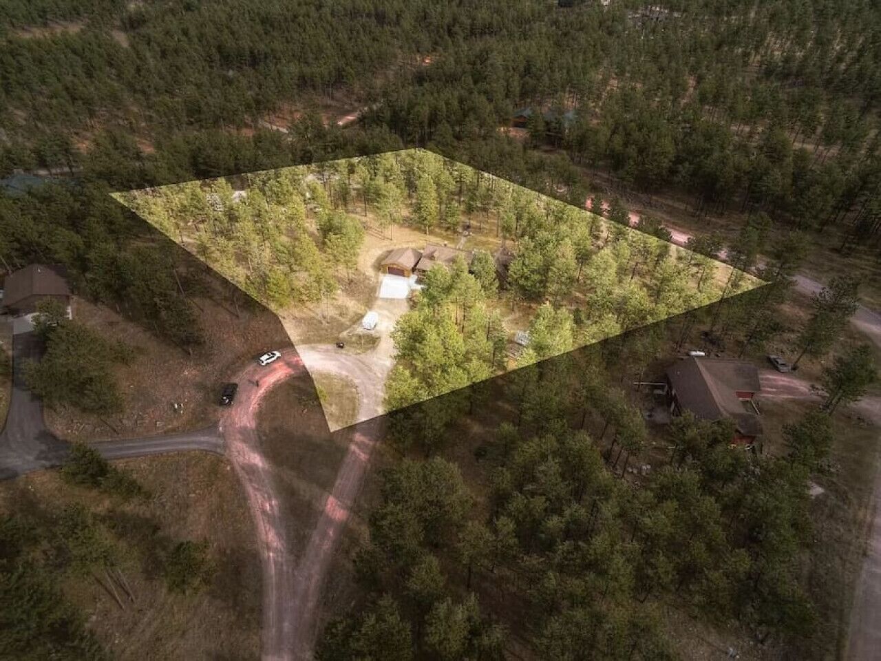 An aerial view of a forested property with a clear rectangular area, possibly for development or construction, surrounded by dense trees and a few buildings.