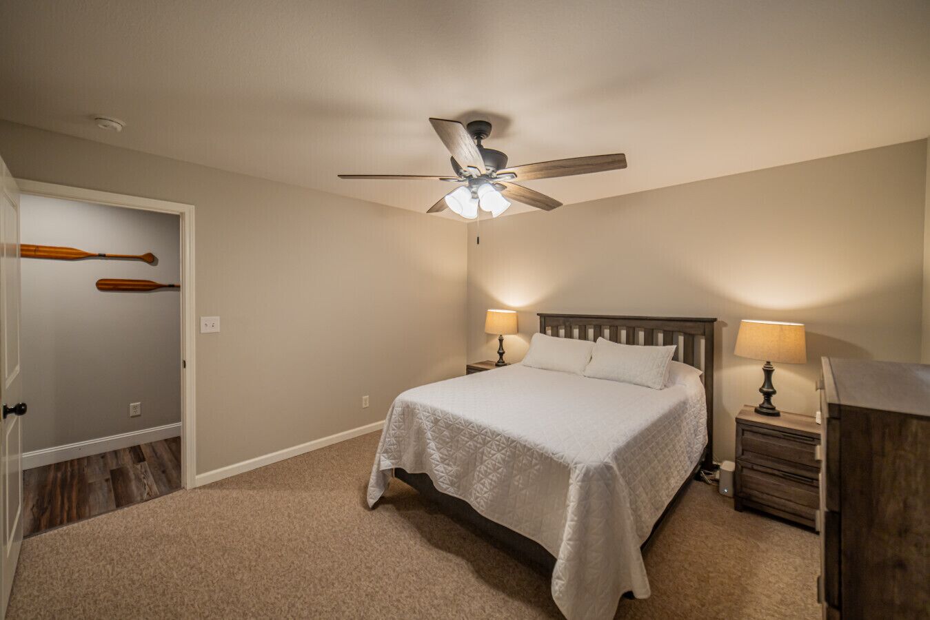 A bedroom with a bed, two bedside tables with lamps, a ceiling fan, and a door with two wooden paddles.