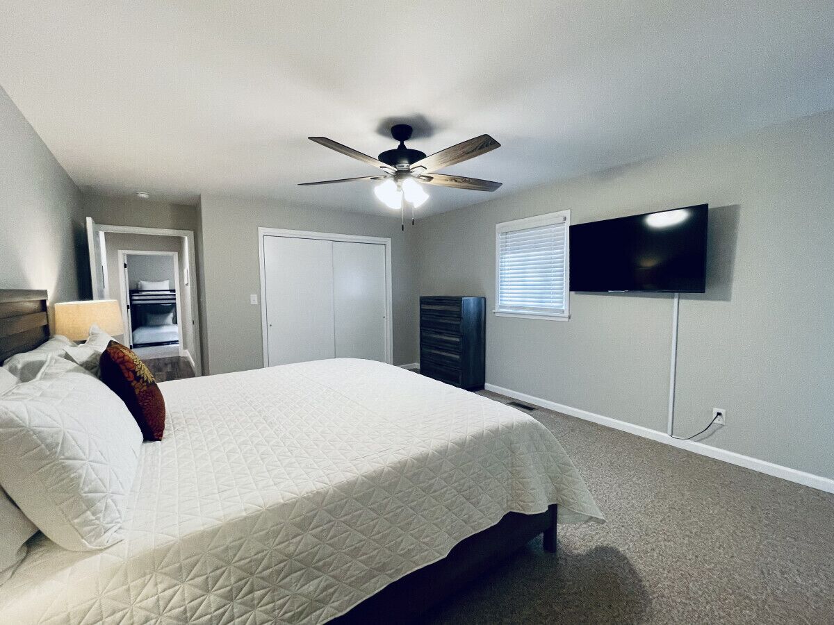 Ein Schlafzimmer mit Bett, Deckenventilator, Fernseher und Kommode.