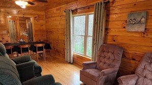 L’intérieur chaleureux d’un chalet comprend un coin repas, deux fauteuils confortables et une fenêtre agrémentée de rideaux.