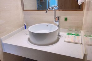 Un baño con un lavabo blanco, un espejo y un dispensador de jabón en la encimera.