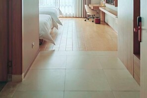 A hotel room with a wooden floor, a bed with white linens, a desk with a chair, and a window with curtains. - Vienna 3 Best Hotel (Huai'an Huaiyin Normal University North Bus Station) (Huai'an)