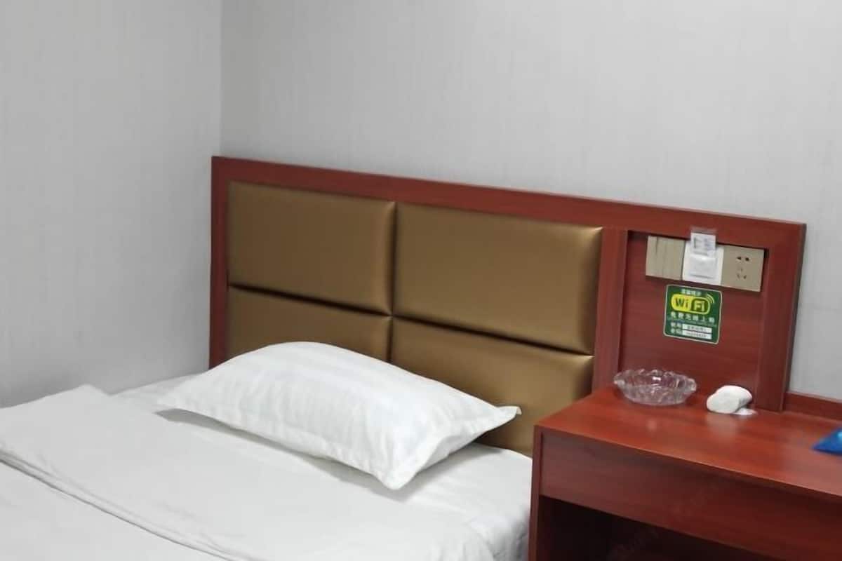 Ein Hotelzimmer mit Bett, Holz-Kopfteil, Nachttisch, W-LAN-Symbol und einer kleinen Dekoration.