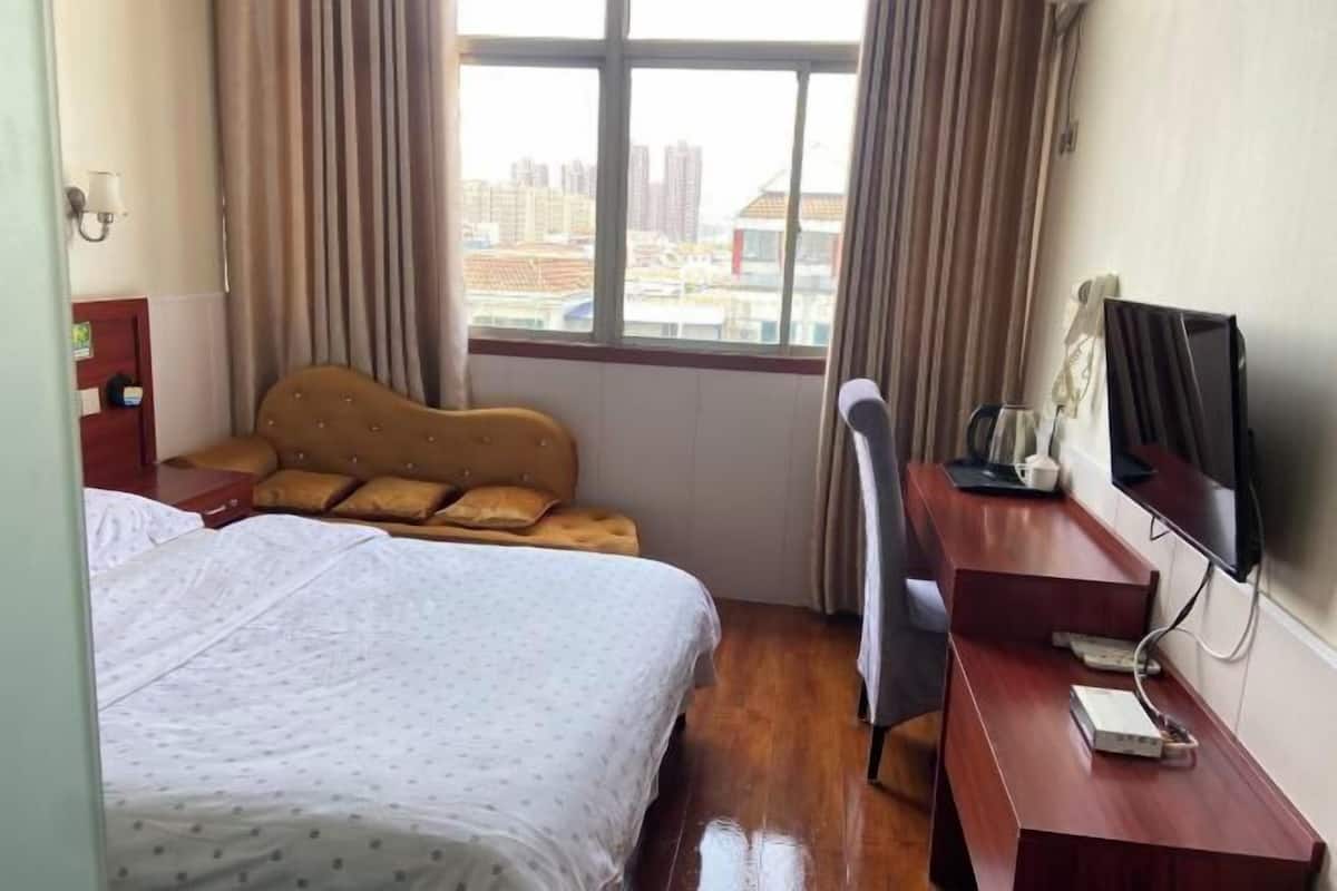 Ein Hotelzimmer mit Bett, Schreibtisch, Stuhl, Fernseher und einem Fenster mit Vorhängen.