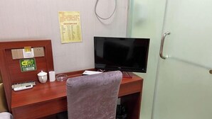 A room with a wooden desk, a television, a chair, a Wi-Fi sign, a menu board, and a door with a handle. - Mengcheng Jiayue Hotel (Mengcheng)