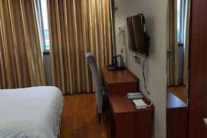 A hotel room with a bed, a desk with a chair, a flat-screen TV, and a window with curtains.