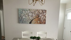 A dining room with a wooden table and chairs, a chandelier, and a floral painting on the wall. - Quaint spacious remodeled home with attached garage, quiet small town get-away (Concordia)