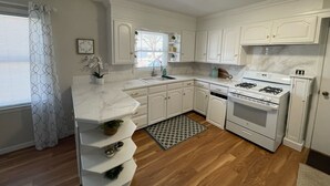 A kitchen with white cabinets, a stove, and a sink. - Quaint spacious remodeled home with attached garage, quiet small town get-away (Concordia)