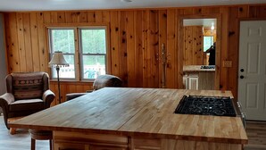 Cocina con paneles de madera, una isla central, zona de comedor con una silla y vistas a través de una ventana.