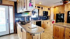 Una cocina con armarios de madera, encimeras de granito, microondas integrado y ventilador de techo.