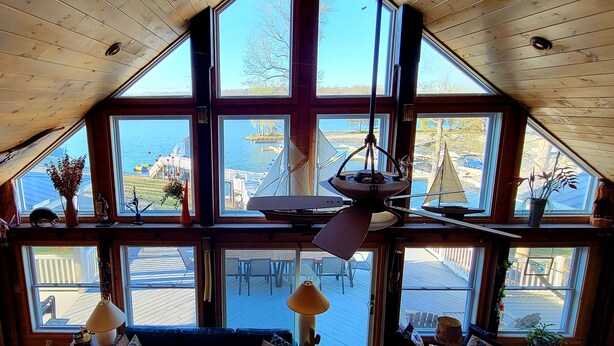 Habitación con techos altos, ventanas amplias, ventilador de techo y vista al muelle y un velero.