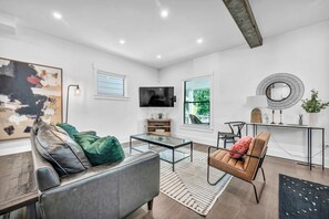 A modern living room with a leather sofa, a glass coffee table, a TV, and a large window.