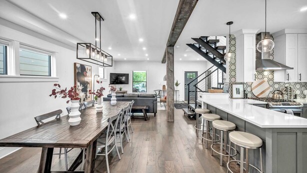 A modern kitchen with a wooden dining table, bar stools, and a staircase leading to an upper level. - Miracle on 54th - Hot Tub, Sauna, and Pickleball (Cleveland)