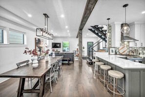 Une cuisine moderne avec une table à manger en bois, des tabourets de bar et un escalier menant à un niveau supérieur.