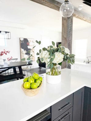 A kitchen counter with a vase of flowers and a bowl of green apples.