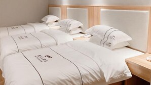 Quarto de hotel com duas camas, cada uma com roupa de cama e almofadas brancas, e cabeceira de madeira.