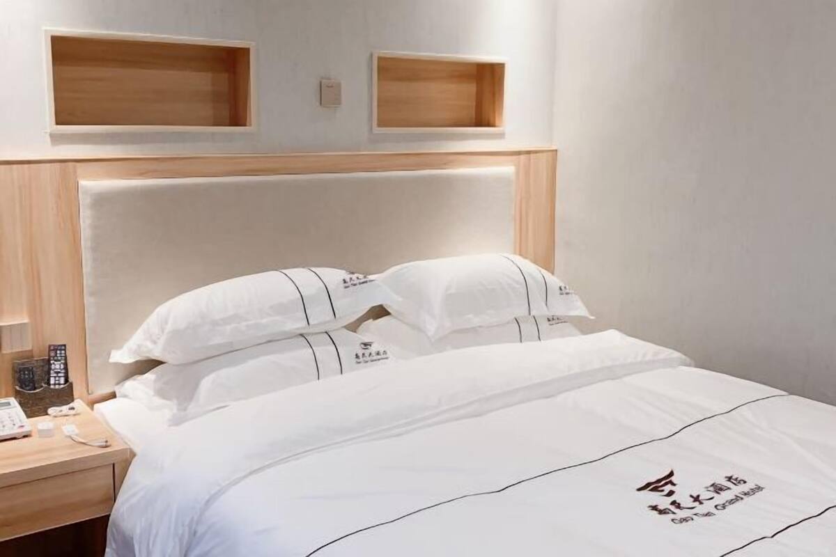 Une chambre d’hôtel avec un lit, une tête de lit en bois, deux tables de chevet et une étagère fixée au mur.