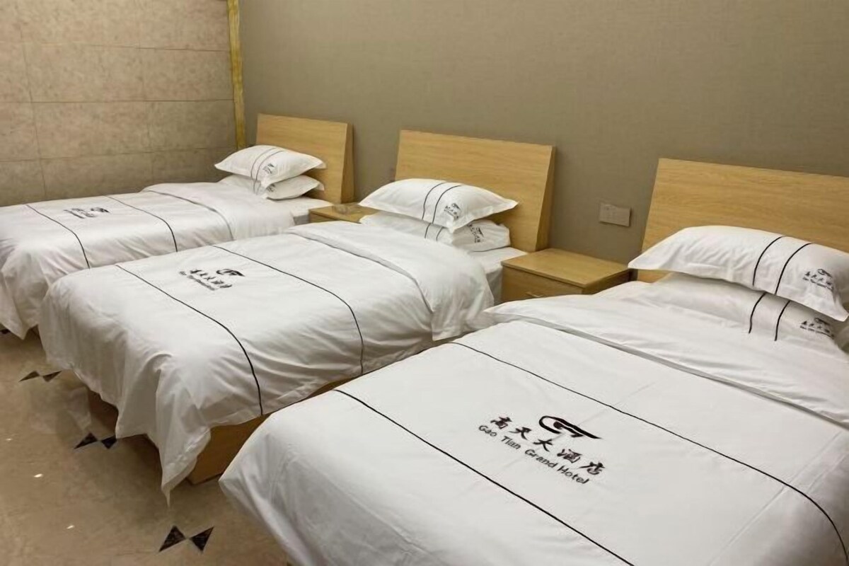 Ein Hotelzimmer mit drei Betten, jedes mit einer weißen Bettdecke mit Logo und Schriftzug.