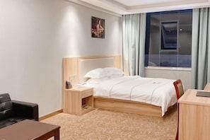 Une chambre d’hôtel avec un lit, un bureau, une chaise, une table de chevet et une fenêtre avec des rideaux.