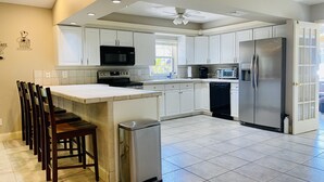 A modern kitchen with white cabinets, a stainless steel refrigerator, a microwave, and a dishwasher. - Vanderbilt Beach Retreat- 4 Bed 1-level, Spacious, & Pet-Friendly - 3 King Beds (Naples)