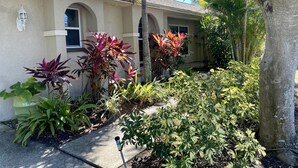 A building with a beige facade, arched windows, and a well-maintained garden with various plants. - Vanderbilt Beach Retreat- 4 Bed 1-level, Spacious, & Pet-Friendly - 3 King Beds (Naples)
